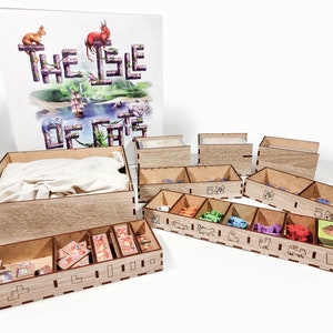 Puede incluir: Organizador de madera para el juego de mesa "The Isle of Cats". El organizador tiene varios compartimentos para guardar los componentes del juego, incluidas las cartas, las fichas y los meeples. El organizador está hecho de madera natural y tiene un acabado marrón claro.