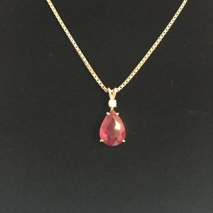 May include: A gold chain necklace with a pear-shaped red gemstone pendant accented with two small diamonds.