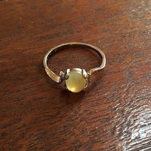 May include: A silver ring with a pale yellow oval-shaped gemstone set in a claw setting.