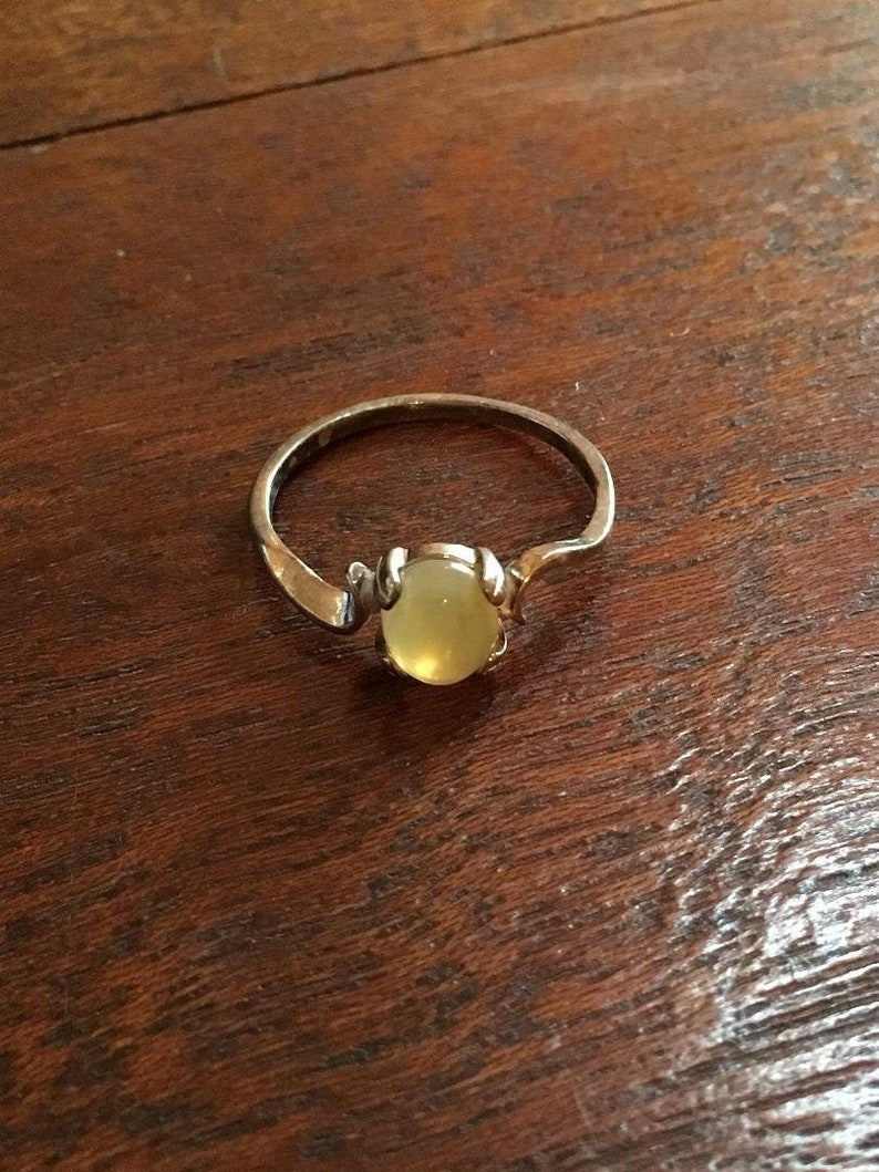 May include: A silver ring with a pale yellow oval-shaped gemstone set in a claw setting.