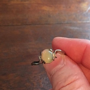 May include: A silver ring with a pale green oval gemstone set in a delicate, curved design.
