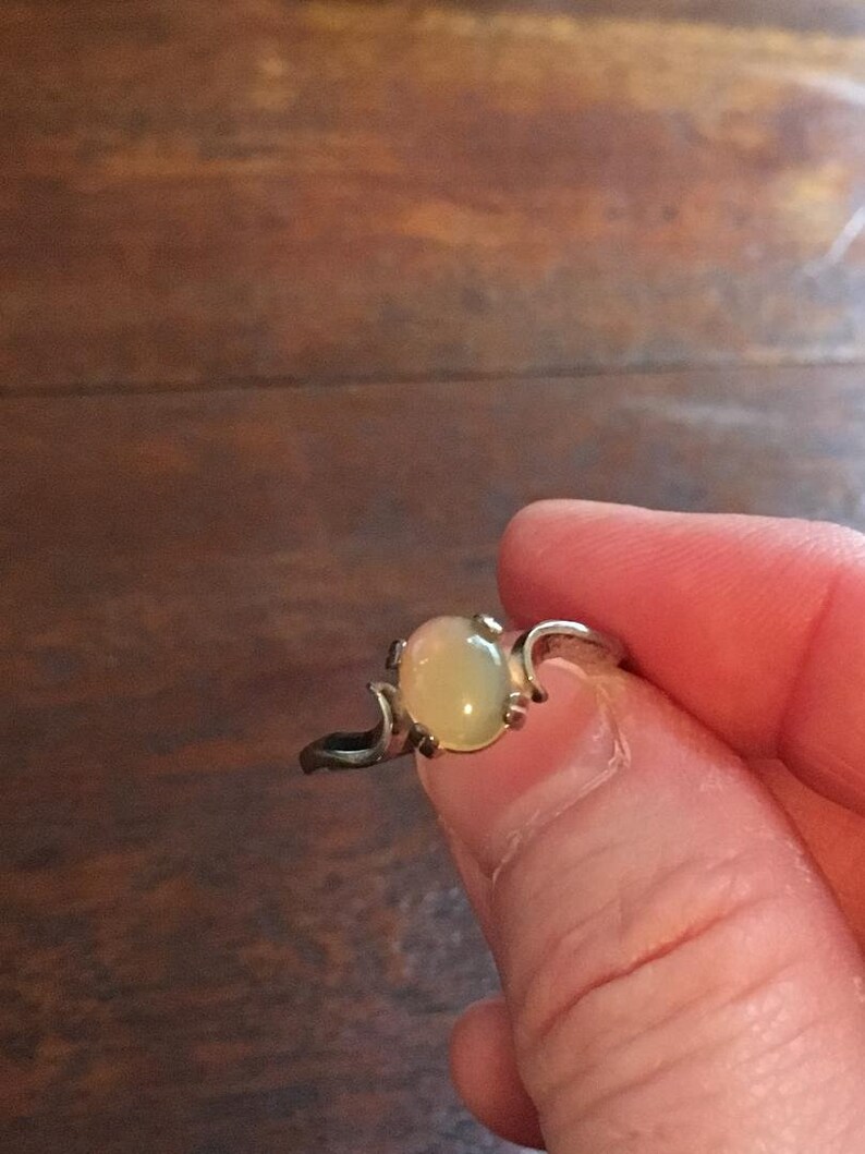 May include: A silver ring with a pale green oval gemstone set in a delicate, curved design.