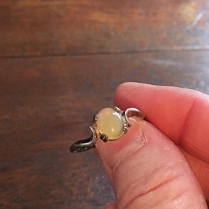 May include: A silver ring with a pale yellow oval opal gemstone. The ring has a delicate, curved design.