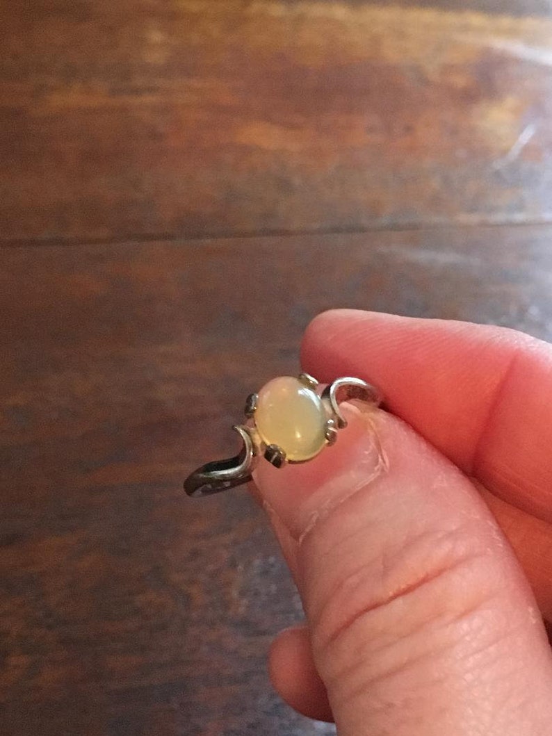May include: A silver ring with a pale yellow oval opal gemstone. The ring has a delicate, curved design.