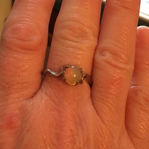 May include: A silver ring with a delicate, curved band and a round, pale yellow opal gemstone.