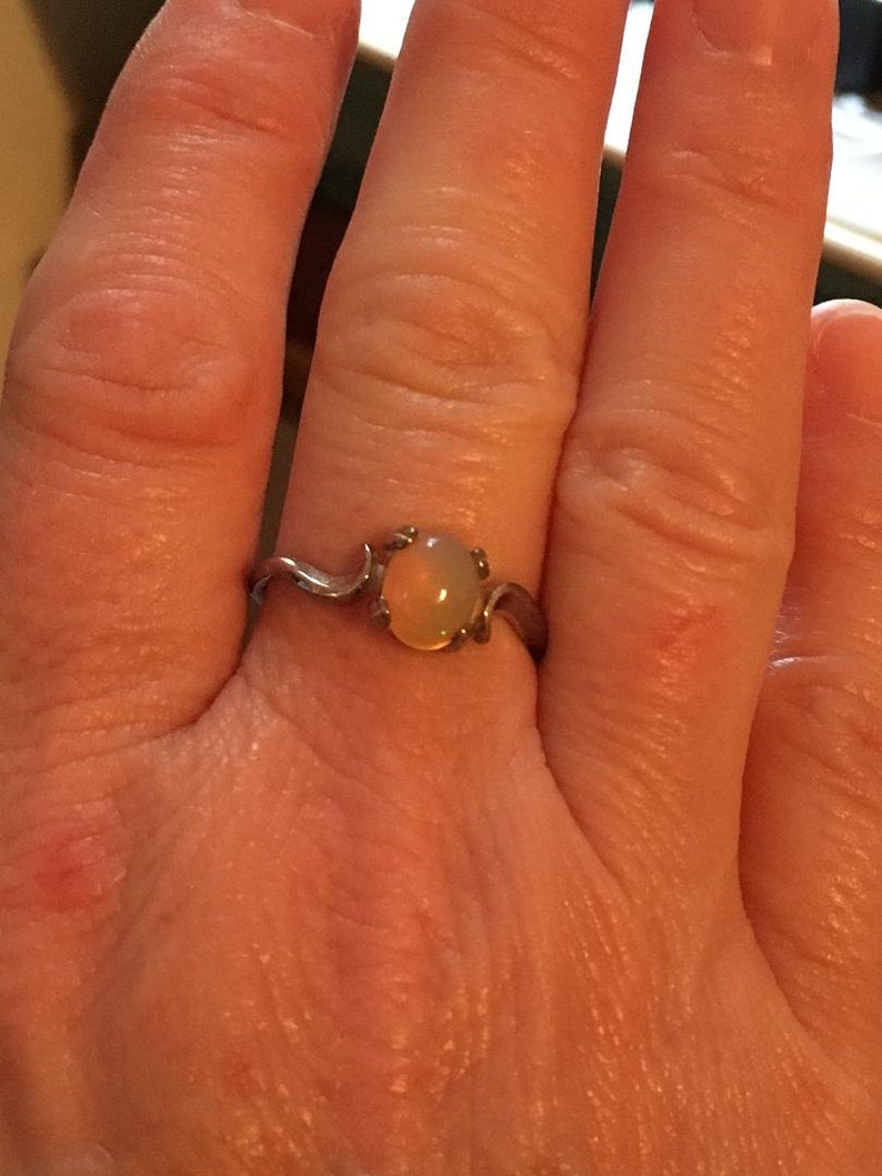 May include: A silver ring with a delicate, curved band and a round, pale yellow opal gemstone.