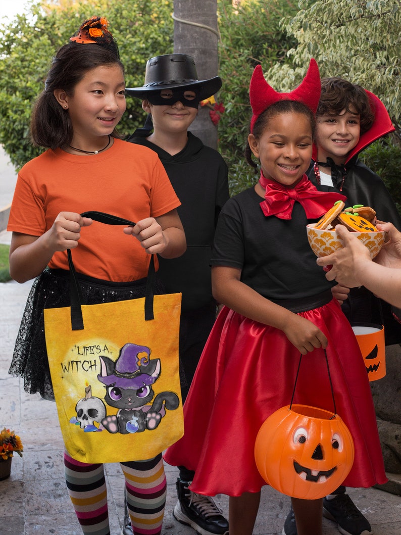 May include: Four children dressed in Halloween costumes, two girls and two boys, are trick-or-treating. One girl is wearing a red devil costume and holding a pumpkin-shaped bucket. Another girl is wearing an orange shirt and a black witch hat and carrying a yellow tote bag with a black cat illustration and the text "Life's a Witch". A boy is wearing a black cowboy hat and a black mask. Another boy is wearing a black cape and a vampire costume.