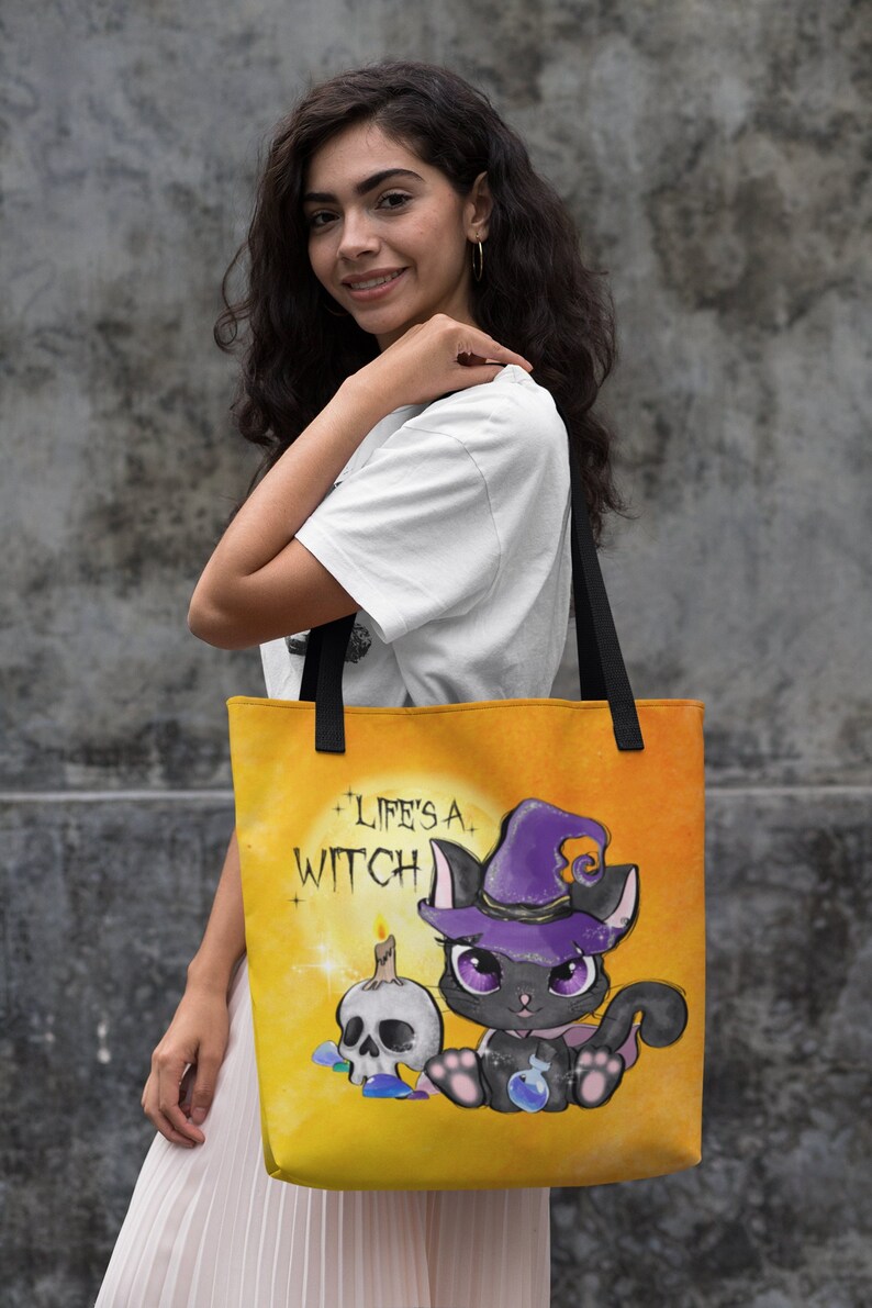 May include: A yellow tote bag with a black cat wearing a purple witch hat and holding a potion bottle. The bag has the text "Life's a Witch" printed on it.