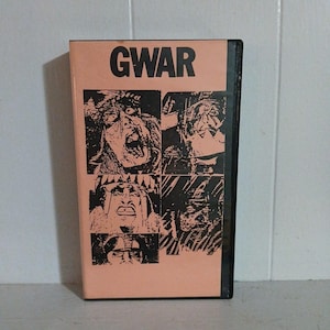 May include: A VHS tape with the word "GWAR" in large black letters at the top. Below the text are four black and white images of grotesque faces. The tape has a peach-colored cover and a black spine.
