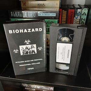 May include: Black VHS tape with a white label that reads "BIOHAZARD" and "DYNAMO OPEN AIR FESTIVAL EINDHOVEN, HOLLAND 1995".