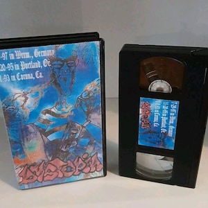 May include: A VHS tape with a black case and a blue and white label. The label has the text "1-29-97 in Werm., Germany", "11-20-95 in Portland, Or", "1-1-93 in Corona, Ca.", "11.93 & Cam, Ca.", "11-20-45 in Borza, θε", and "7-29-97 in см., бесилля".