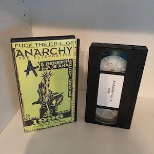 May include: A black VHS tape and case with the text "ANARCHY" and "1996". The case is yellow and black with the text "FUCK THE F.B.I. GET ANARCHY THE ALTERNATIVE". The tape has a white label that reads "ANARCHY Vol. 4 1996".