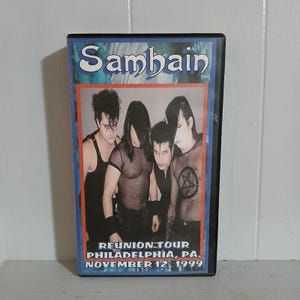 May include: A DVD case featuring the band "Sambain." The cover art displays a group photo of the band members in dark attire. The text "REUNION TOUR PHILADELPHIA, PA. NOVEMBER 12, 1999" is printed at the bottom.