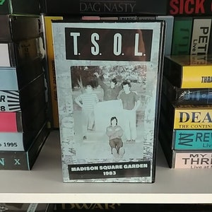 May include: A VHS tape with a black and white photo of a band on the cover. The band is TSOL and the tape is titled "Madison Square Garden 1983".