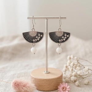 May include: A pair of silver-toned drop earrings featuring a black fan-shaped charm with small clear stones arranged in a floral pattern. Each earring is finished with a single round white bead dangling from the bottom of the fan component.