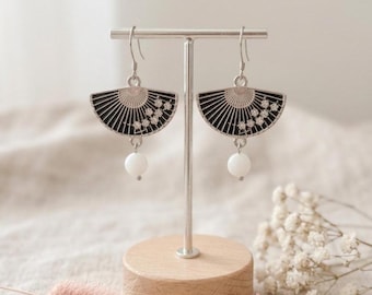 May include: A pair of silver-toned dangle earrings shaped like folding fans. Each fan features a black background with a delicate white floral pattern and a single white bead hanging from the bottom center, suspended on a silver hook wire.