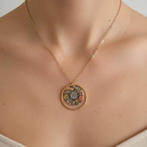 May include: Gold-toned necklace featuring a circular pendant with a floral design. The pendant showcases a colorful arrangement of flowers in shades of blue, orange, and yellow. The necklace is a delicate piece of jewelry.