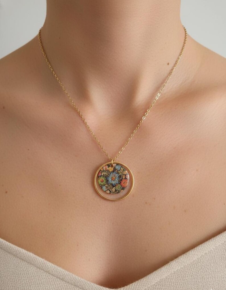 May include: Gold-toned necklace featuring a circular pendant with a floral design. The pendant showcases a colorful arrangement of flowers in shades of blue, orange, and yellow. The necklace is a delicate piece of jewelry.