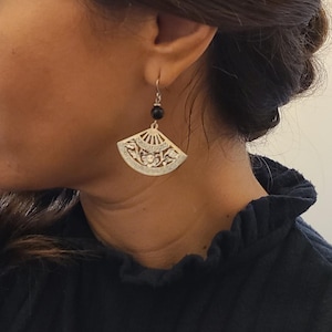 Może przedstawiać: Para srebrnych kolczyków z czarną koralikiem i wzorem w kształcie wachlarza.