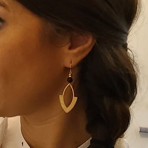 May include: Gold geometric earrings with a black bead accent. The earrings are dangling and have a teardrop shape.
