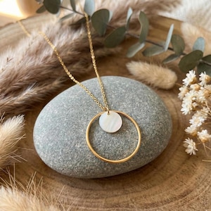 May include: A gold-toned necklace featuring a delicate chain and a pendant composed of a large, thin gold-toned circle framing a smaller, iridescent white circular disc made of mother-of-pearl, creating a layered and geometric aesthetic.