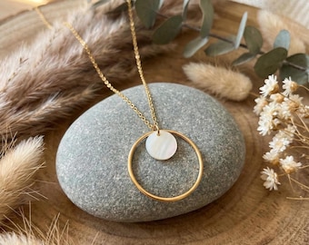 May include: A gold-toned necklace featuring a delicate chain and a pendant composed of a large, thin gold-toned circle framing a smaller, iridescent white circular disc made of mother-of-pearl, creating a layered and geometric aesthetic.