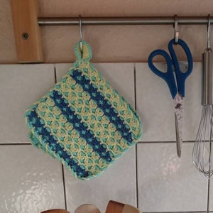 Pode incluir: Um jarro de bolinhas cinzas e brancas com um design de coração e uma alça. O jarro está cheio de colheres de madeira e está sentado em um balcão. Há outros itens de cozinha pendurados em uma grade acima do jarro, incluindo um pegador de panela de crochê azul e verde, um par de tesouras azuis e um batedor de arame prateado.