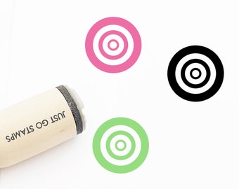 May include: Three wooden stamps with a target design. The stamps are in pink, green, and black. The text "JUST GO STAMPS" is printed on the side of one of the stamps.