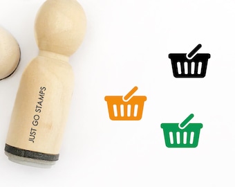 May include: Wooden stamp with the text "JUST GO STAMPS" and a black and white image of a shopping basket. The stamp is on a white background. There are also images of orange and green shopping baskets.