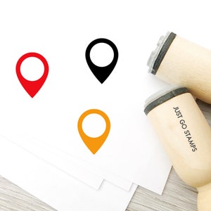 May include: Three wooden stamps with different coloured location pin designs. The stamps are labelled "Just Go Stamps".