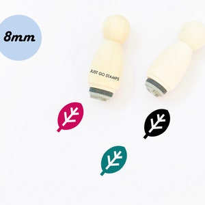 Op de afbeelding: Drie houten stempels met een bladerenontwerp. De stempels hebben een diameter van 8 mm en zijn verkrijgbaar in zwart, groen en roze. De stempels zijn gelabeld met "JUST GO STAMPS".