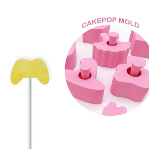 May include: Pink cake pop mold with various shapes, including a ballerina, a crown, and a heart. The mold is made of silicone and is designed to create cake pops that are easy to remove. CAKEPOP MOLD is written in pink letters on the mold.