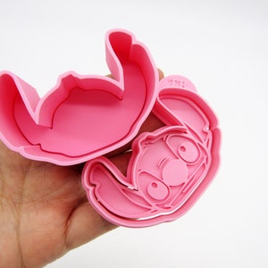 May include: Pink plastic cookie cutter shaped like Stitch from the Disney movie Lilo & Stitch. The cutter is in two pieces, one for the outline and one for the details.