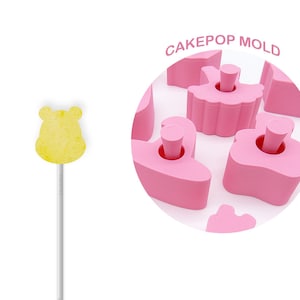 May include: Pink cake pop mold with different shapes, including a ballerina, a heart, and a flower. The mold is made of silicone and is designed to create cake pops that are easy to remove. CAKEPOP MOLD is written in white letters on a pink circle.