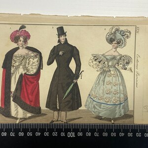 May include: A vintage fashion illustration from 1831 depicting three people in fashionable attire. The woman on the left wears a white dress with a red shawl and a pink hat. The man in the middle wears a black coat and a top hat. The woman on the right wears a light blue dress with a large white hat and a blue sash.