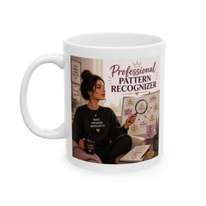 May include: A white ceramic mug featuring a graphic illustration of a person in a black sweatshirt holding a magnifying glass over a whiteboard. The text reads Professional Pattern Recognizer, Aware Empowered Unapologetic, and I choose peace.