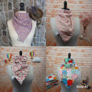 May include: A collection of four triangular fabric bibs displayed on mannequins. The bibs feature various patterns including light purple with small animals, pink with floral prints, hot air balloons, and a colorful patchwork design.