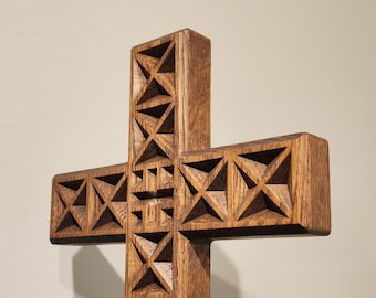 May include: A wooden cross with a geometric design carved into the surface. The cross is made of dark brown wood and has a simple, elegant design.