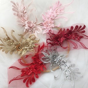 May include: Five different lace appliques with pearl and sequin embellishments. The appliques are in shades of pink, gold, red, silver, and burgundy.