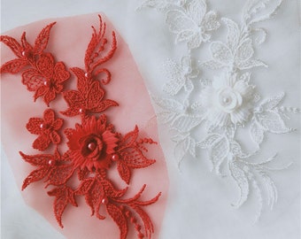 May include: Two floral lace appliques, one red and one white, with pearl-like embellishments. The appliques are on a sheer fabric background.