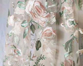 Op de afbeelding: Beige tule stof met geborduurde bloemenmotieven in tinten van groen en roze.