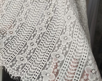 May include: White lace fabric with a delicate floral pattern. The lace has a scalloped edge and a slightly textured surface.