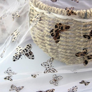 Könnte beinhalten: Weißer, durchsichtiger Stoff mit einer zarten Netzstruktur und einem sich wiederholenden Muster aus braunen und schwarzen Leoparden-Schmetterlingen.