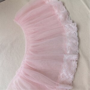 May include: A pink tulle fabric with a white lace trim. The tulle is gathered and ruffled, creating a delicate and feminine look.