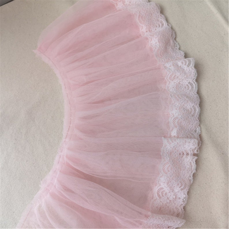 May include: A pink tulle fabric with a white lace trim. The tulle is gathered and ruffled, creating a delicate and feminine look.