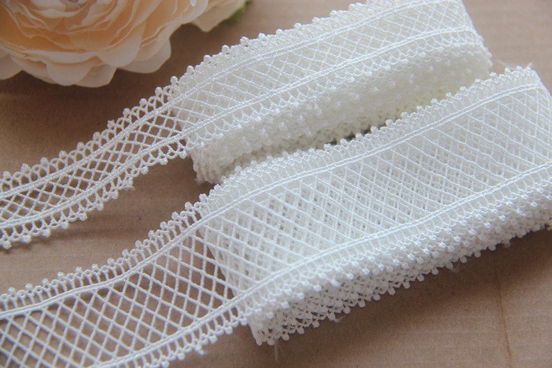 May include: White crochet lace trim with a delicate diamond pattern. The lace is approximately 1 inch wide and has a scalloped edge.