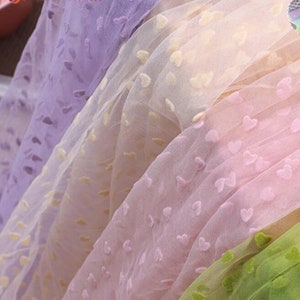 May include: Four pieces of sheer fabric with a heart pattern. The fabric is in shades of purple, pink, yellow, and green.