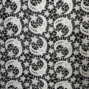 May include: White lace fabric with a repeating pattern of crescent moons and stars. The delicate design features intricate details and a contrasting black background, creating a celestial theme. This textile is suitable for various craft projects.