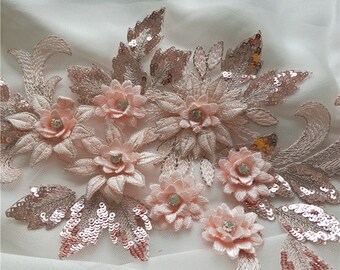 May include: Pink floral embroidery with sequins and rhinestones on a white mesh fabric. This delicate embellishment is perfect for adding a touch of elegance to clothing, accessories, or home decor.