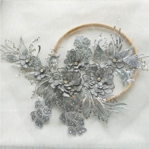 May include: Silver floral applique with sequins and rhinestones. The applique is on a white background and is perfect for adding a touch of sparkle to any project.